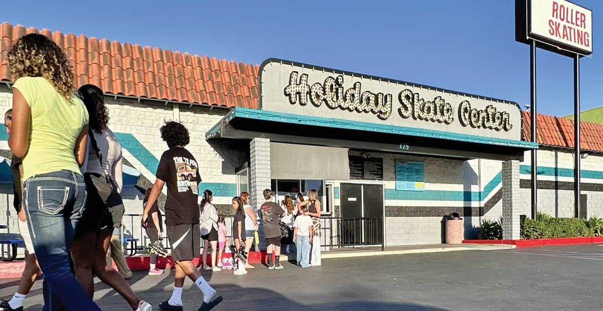 The Holiday Skate Center entrance with its lit marquee sign and a line of skaters, and a Roller Skating sign on a pole