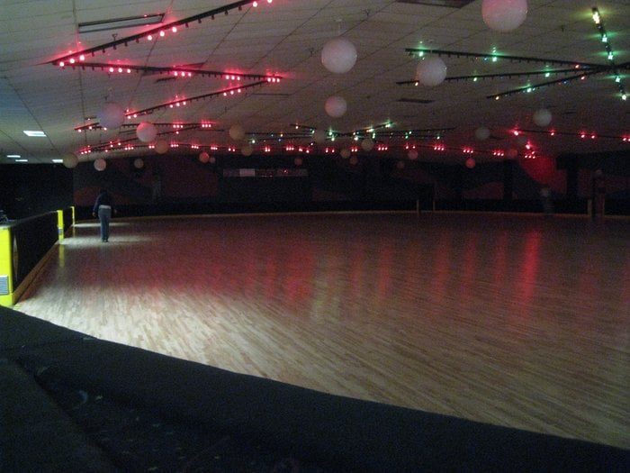 The Skate Depot rink floor at night with red and green lights strung across the ceiling and white globe lights, and a skater near the rail