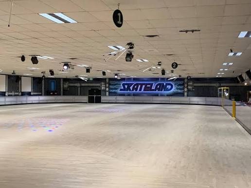 The wide wooden skating floor at Skateland in Northridge under a ceiling of lights, with the blue Skateland sign glowing on the far wall